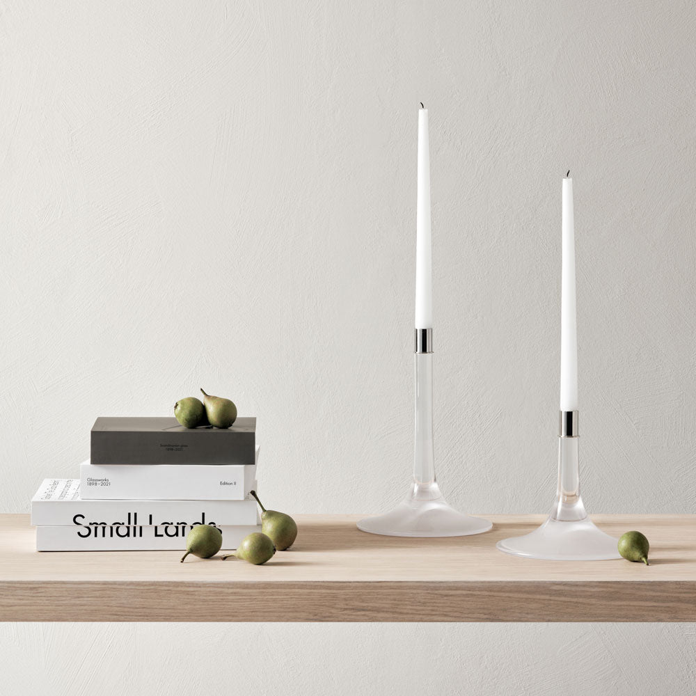 Two Cirrus Candlesticks, Medium by Orrefors a lit white candle, on a wooden home counter