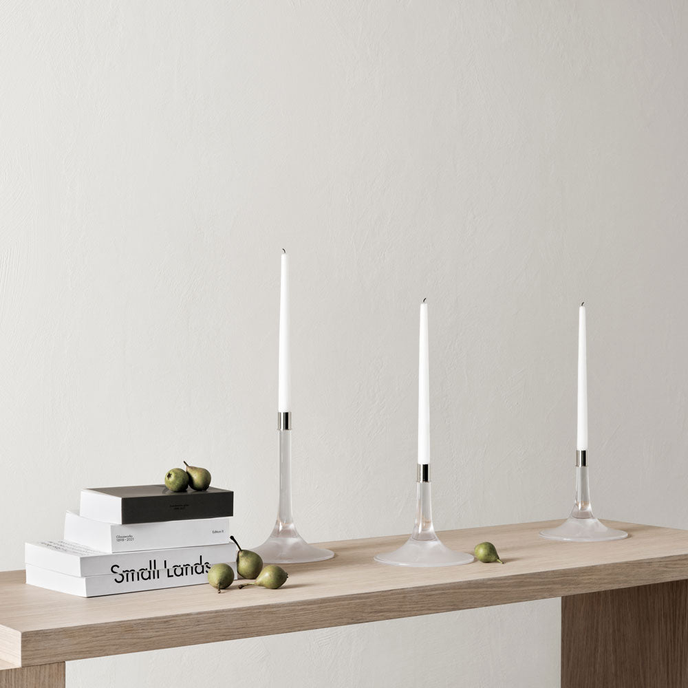 Three Cirrus Candlesticks, Medium by Orrefors a lit white candle, on a wooden home tabletop setting.