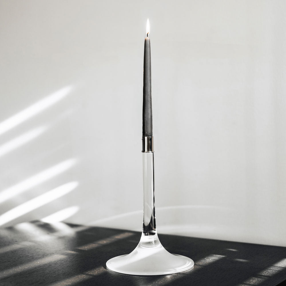 Cirrus Candlestick, Tall by Orrefors holding a lit black candle on a counter