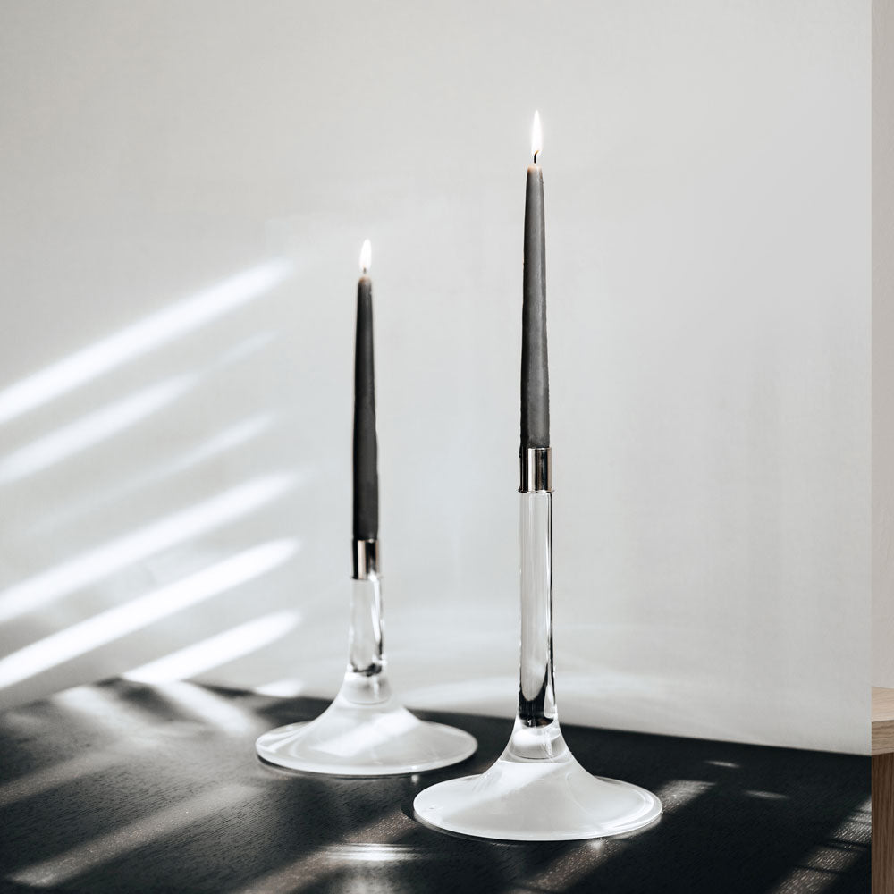Two Cirrus Candlesticks, Tall by Orrefors holding a lit black candle on a counter