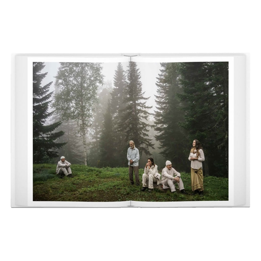 Spread shot of Jonas Bendiksen: The Last Testament, showing a full-width photo of people sitting on grass in the forest