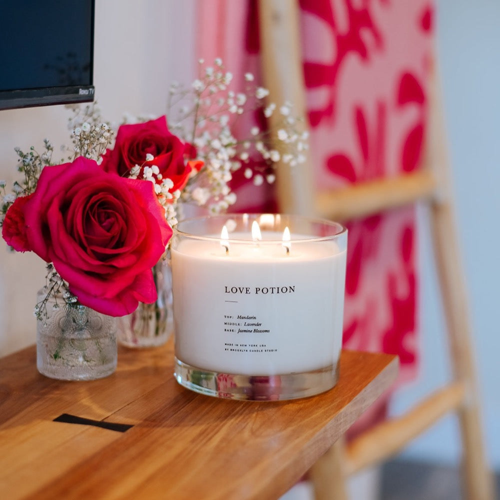 Love Potion Maximalist 3-Wick Candle, lit on a shelf with roses