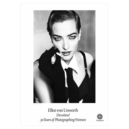 Black and white portrait of Tatjana, dressed in a tie, holding a cigarette, looking confidently at viewer. Exhibition title below: Ellen Von Unwerth | Devotion! 30 Years of Photographing Women