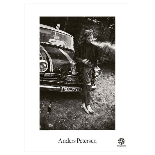 Black and white image of person leaning against car, smoking his cigarette. Artist name below: Anders Petersen