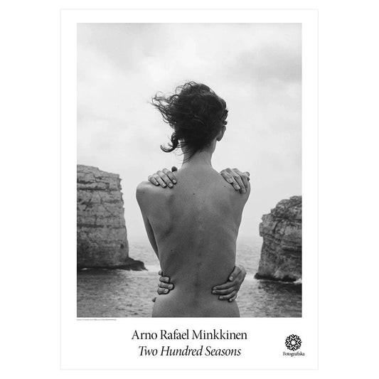 Black and white image of woman looking out at water and rocks with hands on her shoulder and waist. Exhibition title below: Arno Rafael Minkkinen | Two Hundred Seasons