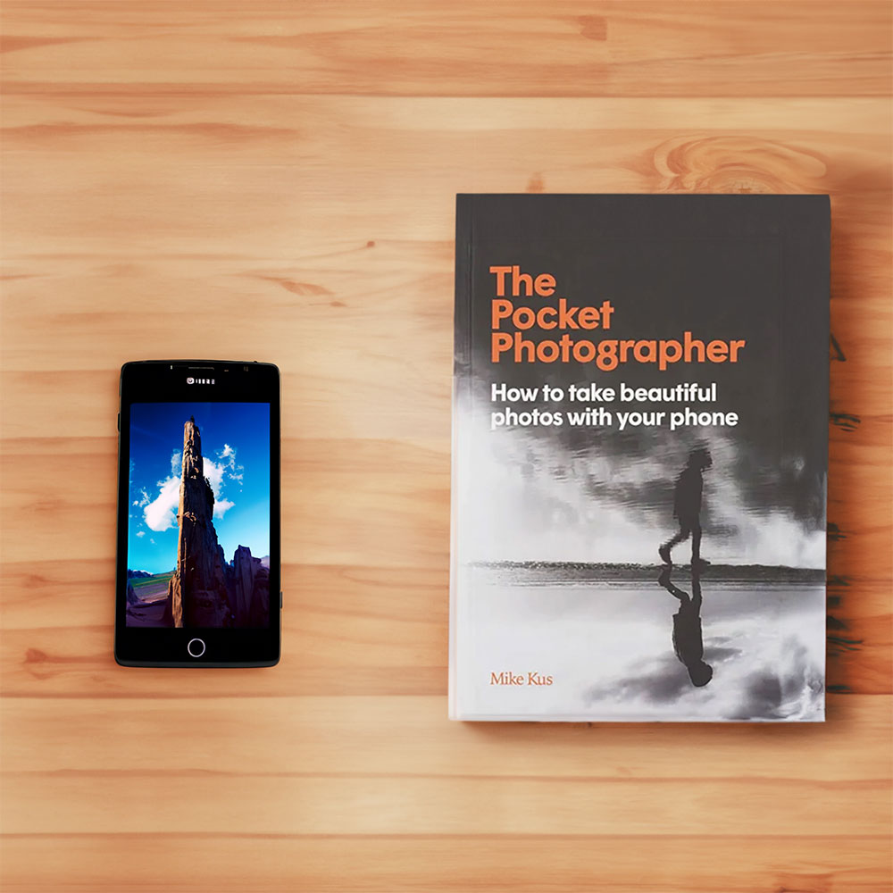Book cover of Pocket Photographer: How to take beautiful photos with your phone, on a wooden desk next to a cell phone showing nature photos.