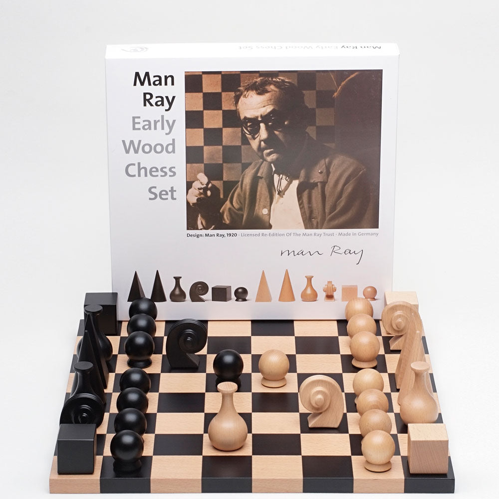 Elegantly designed chess set with abstract chess pieces. Next to packaging showing portrait of Man Ray