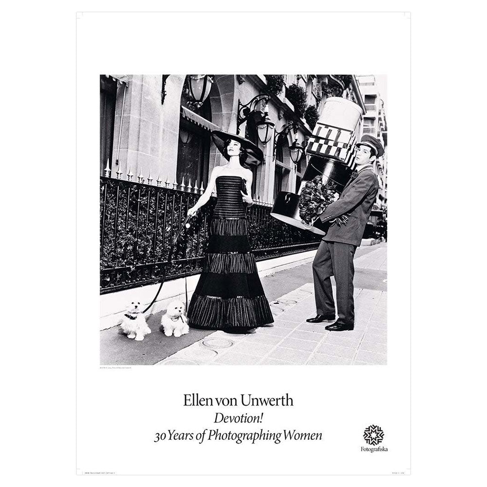 Black and white image of well-to-do woman walking two small designer dogs on a street with doorman lugging heavy object behind her. Exhibition title below: Ellen Von Unwerth | Devotion! 30 Years of Photographing Women