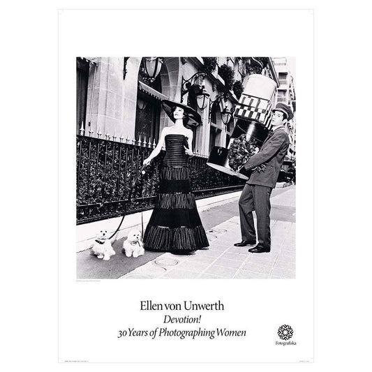Black and white image of well-to-do woman walking two small designer dogs on a street with doorman lugging heavy object behind her. Exhibition title below: Ellen Von Unwerth | Devotion! 30 Years of Photographing Women