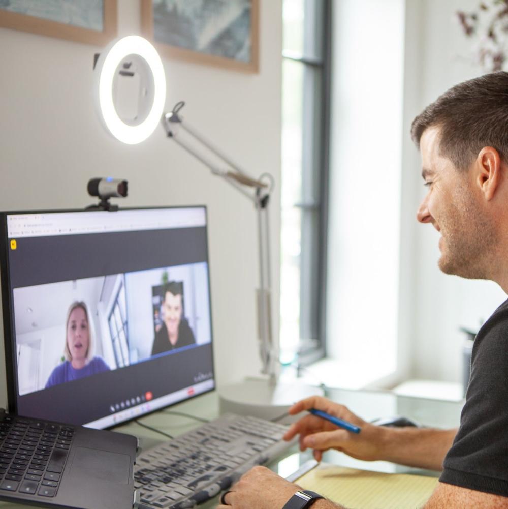 Man using the white Canvas lamp to improve he lighting by his computer for a virtual call.