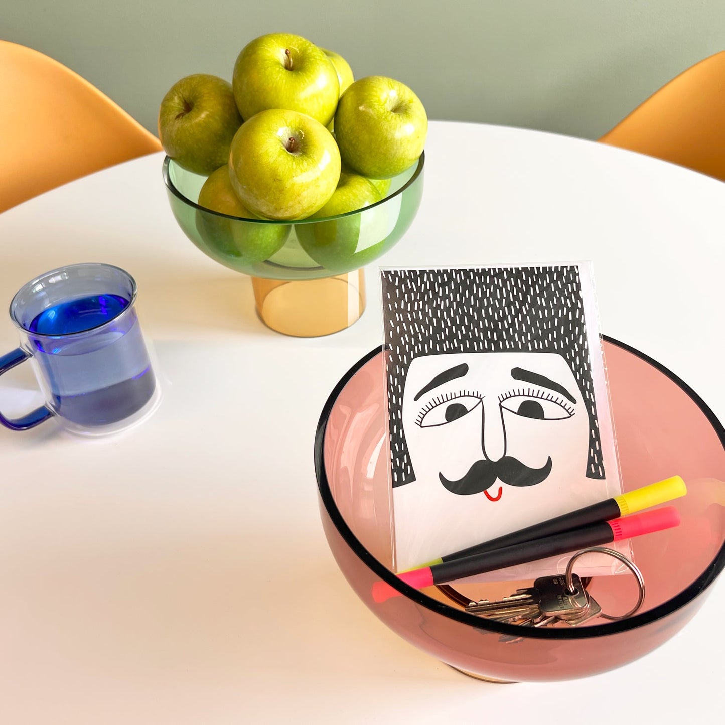 Tip Top Glass Bowl by Cloudnola, in green and yellow, shown holding apples on a colorful table.