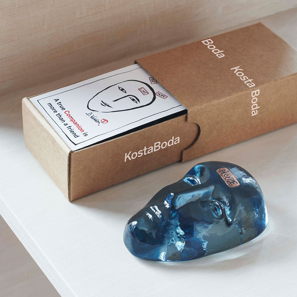 Blue glass face with the word "Hope" on the forehead, laying down next to its packaging.