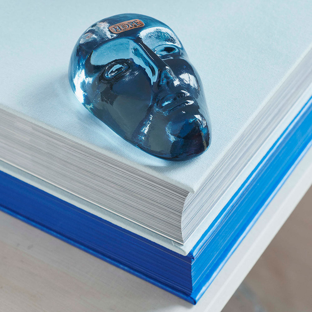 Blue glass face with the word "Hope" on the forehead, laying on a white book.