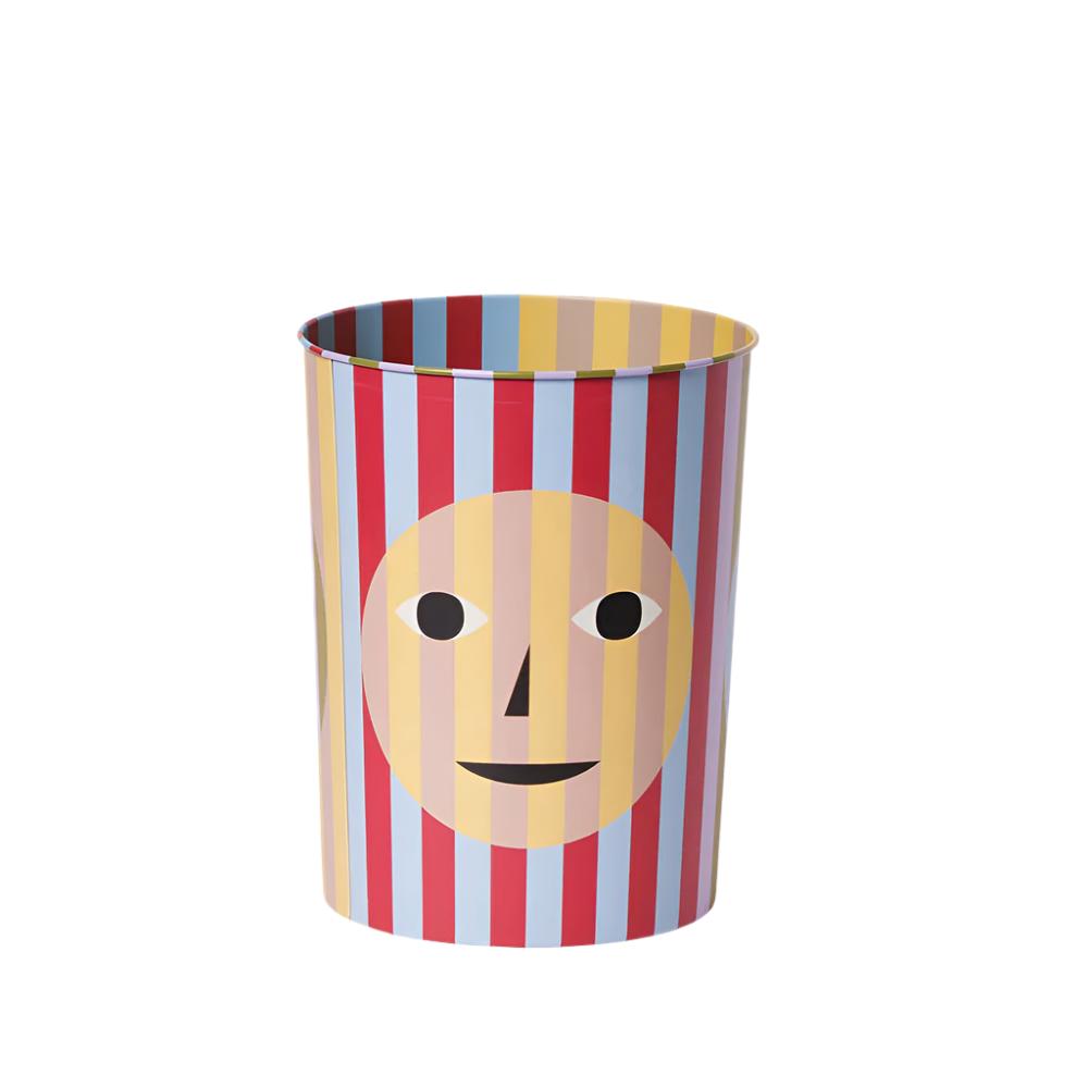 Trash bin with a fun a quirky design - blue and red stripes behind a transparent yellow smiley face