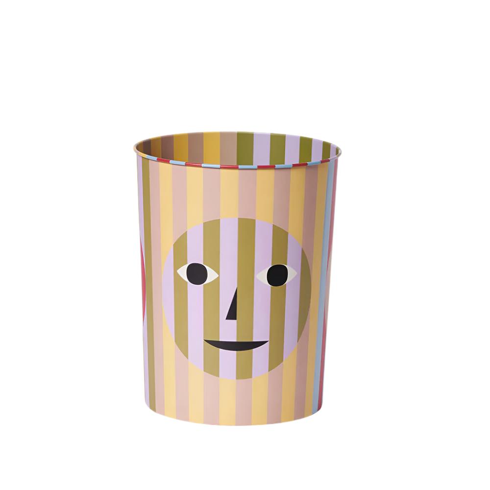 Trash bin with a fun a quirky design - beige and yellow stripes behind a transparent smiley face