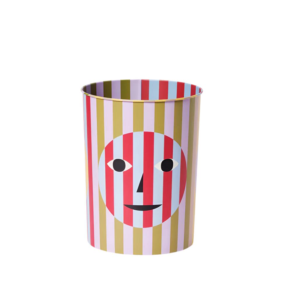 Trash bin with a fun a quirky design - pink and green stripes behind a transparent smiley face 