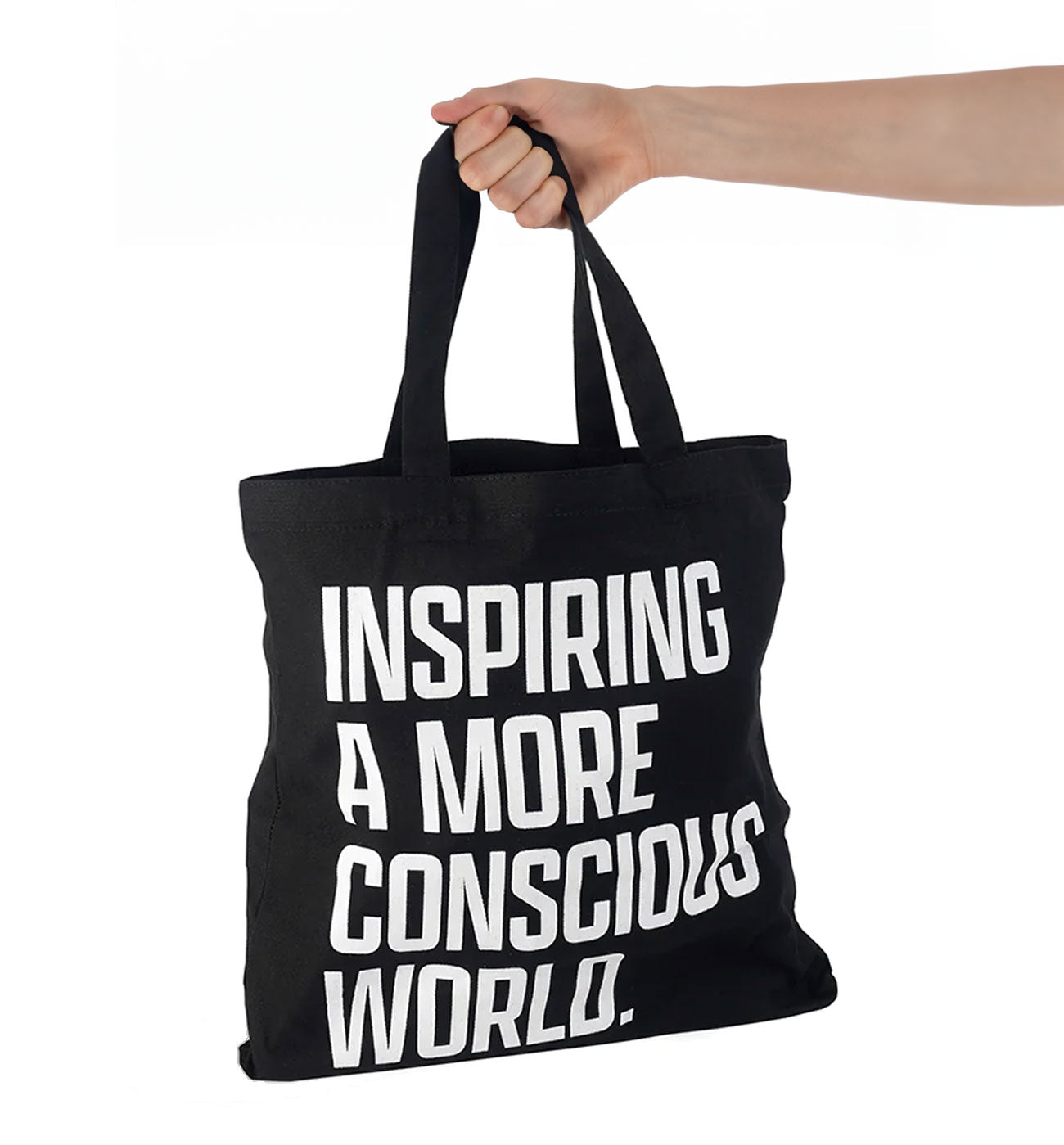 Hand holding "Inspiring a More Conscious World" tote bag.