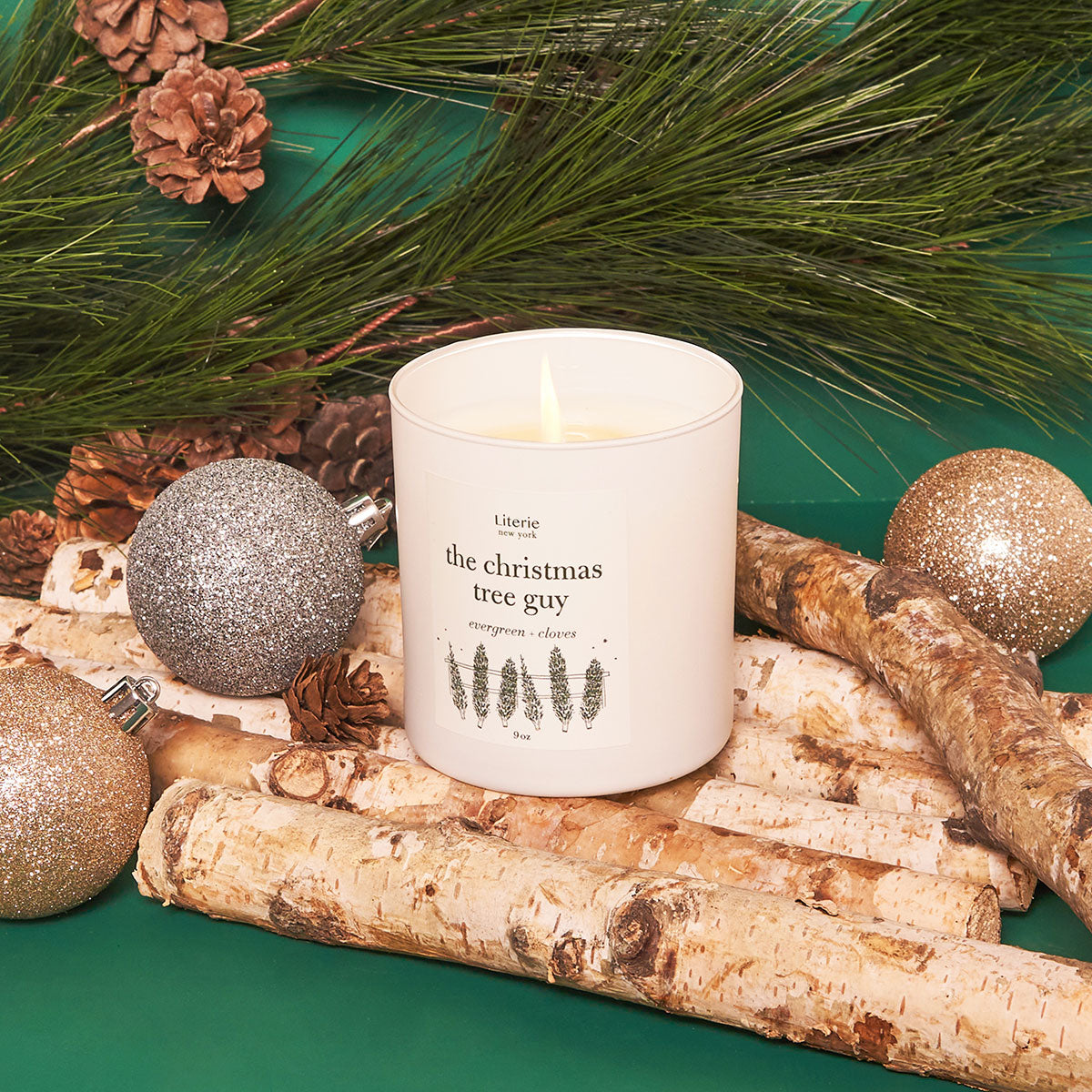 The Christmas Tree Guy Candle candle by Literie - notes of evergreen and cloves, next to some holiday decorations.