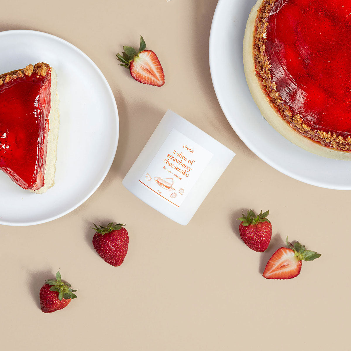 Literie's "A Slice of Strawberry Cheesecake" candle, shown on a table with strawberry cheesecake and strawberries.